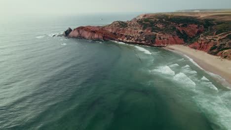 coastal view of a beach with red rocks and waves