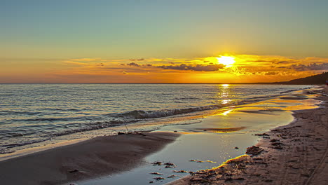 lapso de tiempo de amanecer vibrante a lo largo de la costa, pequeñas olas rompen en la playa de arena