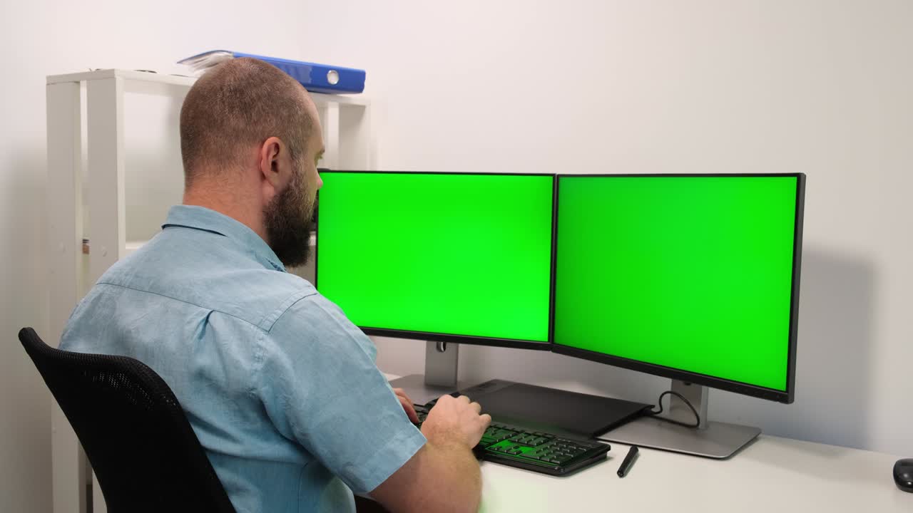 freelancer Working on a Computer, Two Monitor Screens Show Chroma Key. Green Screen and Spreadsheet Software Display. a man typing on a keyboard at home in self-isolation and quarantine