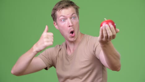 young handsome scandinavian man holding apple and giving thumbs up