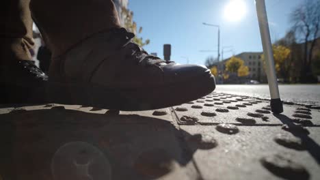 hombre ciego solitario detectando azulejos táctiles, caminando hacia un peatón que cruza una carretera segura