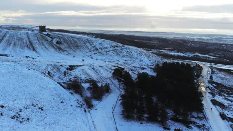 snowy rivington pike tower winter hill vista aérea gente en trineo cuesta abajo al amanecer desplazamiento lento a la izquierda