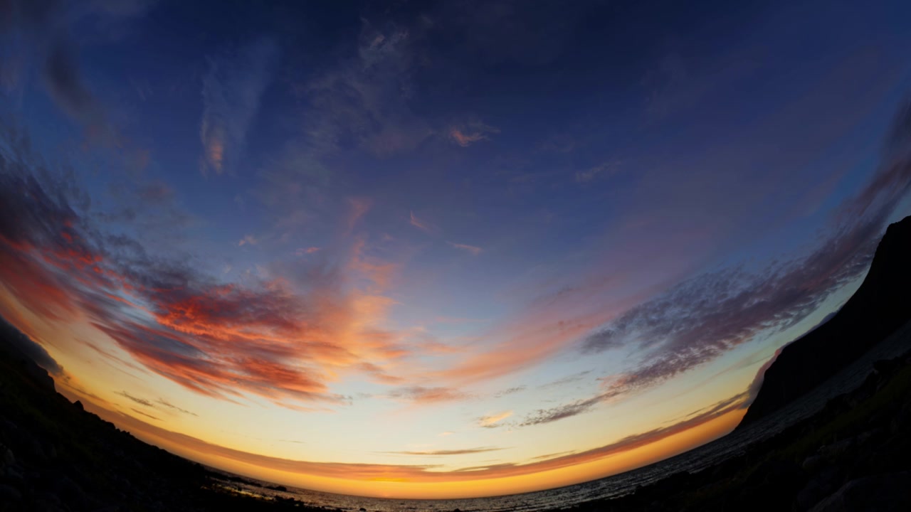 Cielo blu e tramonto nuvoloso sul mare e sulla costa montuosa, visto attraverso un obiettivo fisheye grandangolare da 185° puntato verso l'alto. Flakstad, Isole Lofoten, Norvegia settentrionale