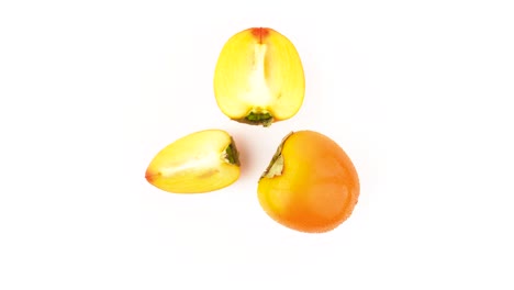 top view from above of a one persimmon fruit with two kaki halves. water drops. rotating. isolated on the white background. close-up. macro.