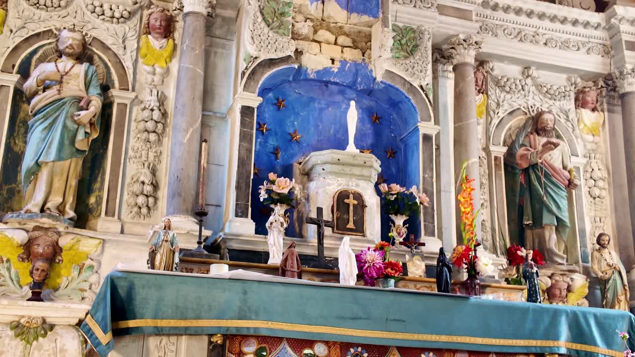 Camera pans upward inside an old chapel in Laval, Mayenne, France, revealing religious statues, the Virgin Mary, and restored ornaments