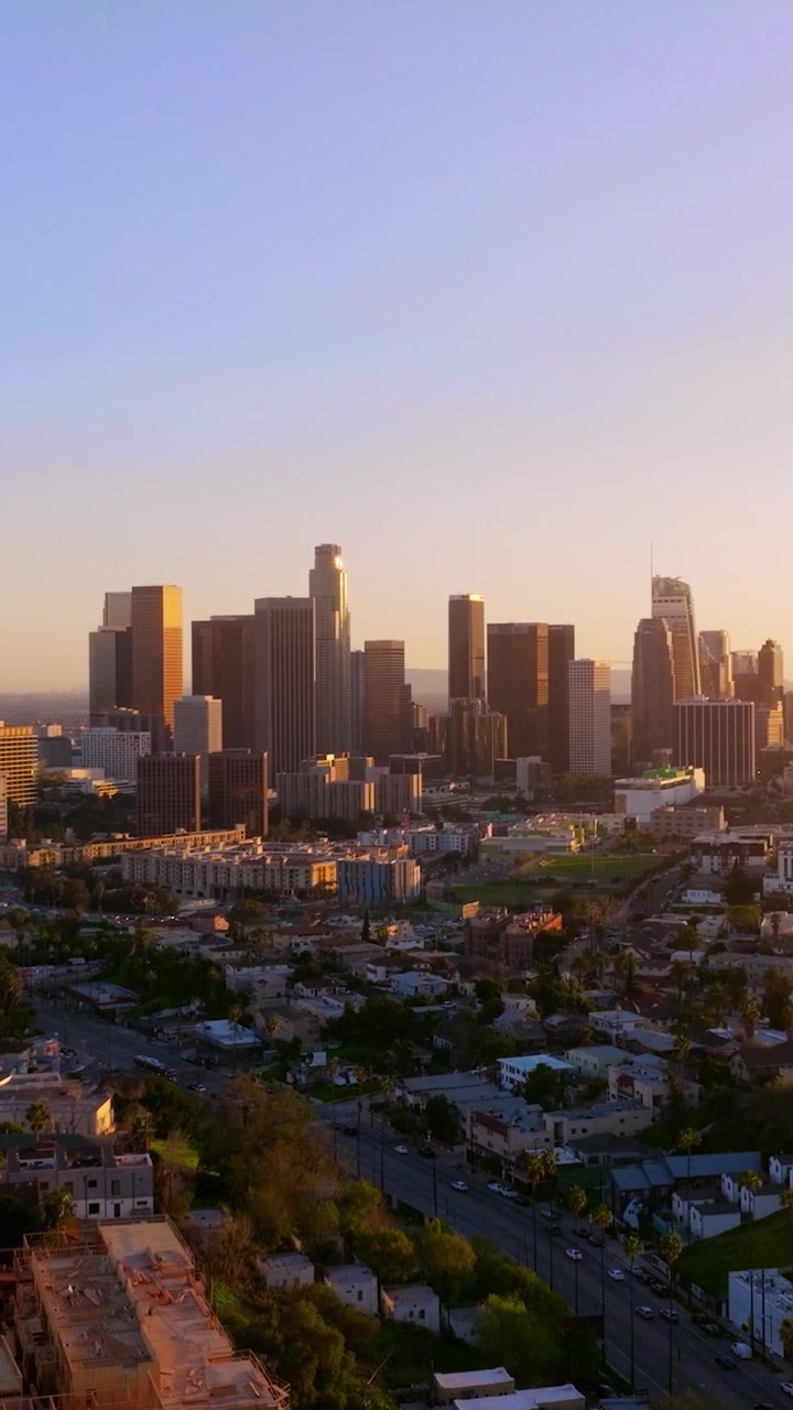 Vista dello skyline di Los Angeles con grattacieli e torri per uffici al tramonto. Congestione del traffico sulle strade durante l'ora di punta. Palme e paesaggio urbano visibili.