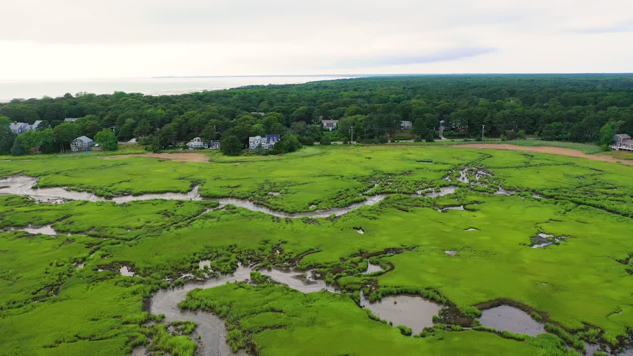 Aerial footage reveals vast marshland with reflective pools and winding creeks, where green grasses and sandy patches weave together into natural patterns visible only from above