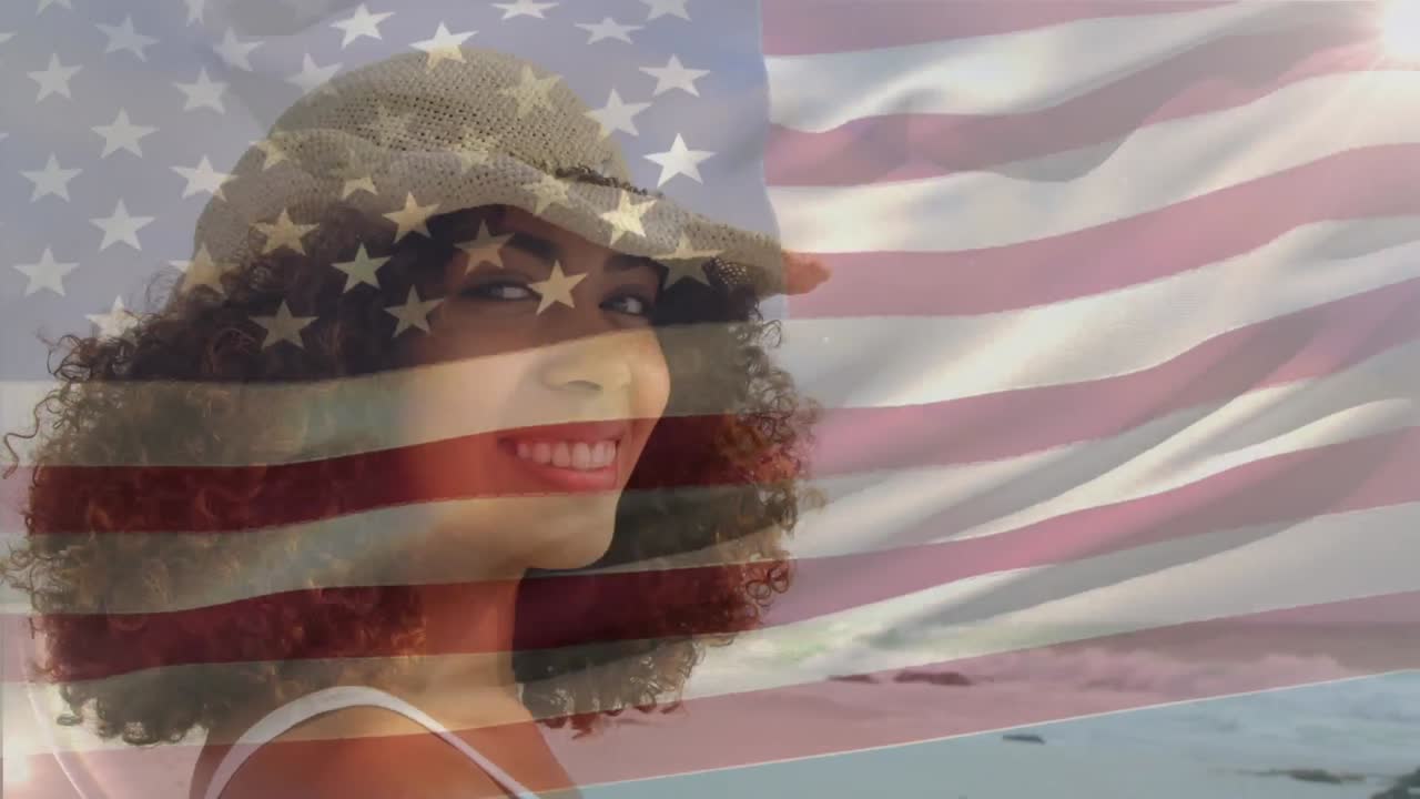 animación de la bandera de américa ondeando sobre una mujer afroamericana sonriente disfrutando de la brisa en la playa