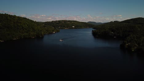 aerial shot of boat on lake doing zigzags surrounded by mountains and clouds on a summer day, backward dolly