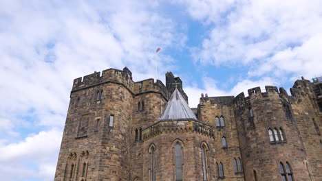 Bandera-Británica-Ondeando-En-La-Cima-Del-Castillo-Medieval-De-Alnwick,-Inglaterra,-Cámara-Lenta-De-ángulo-Bajo