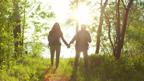 Liebendes-Touristenpaar,-Das-Händchen-Hält,-Lächelt-Und-Spricht,-Während-Es-Bei-Sonnenuntergang-Durch-Den-Grünen-Wald-Geht