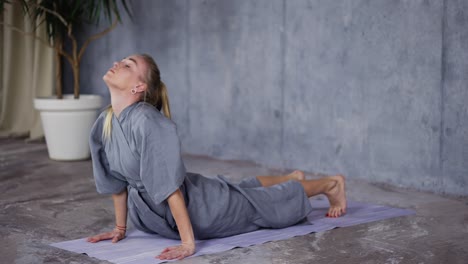 mujer rubia en túnica elegante haciendo yoga en el tapete