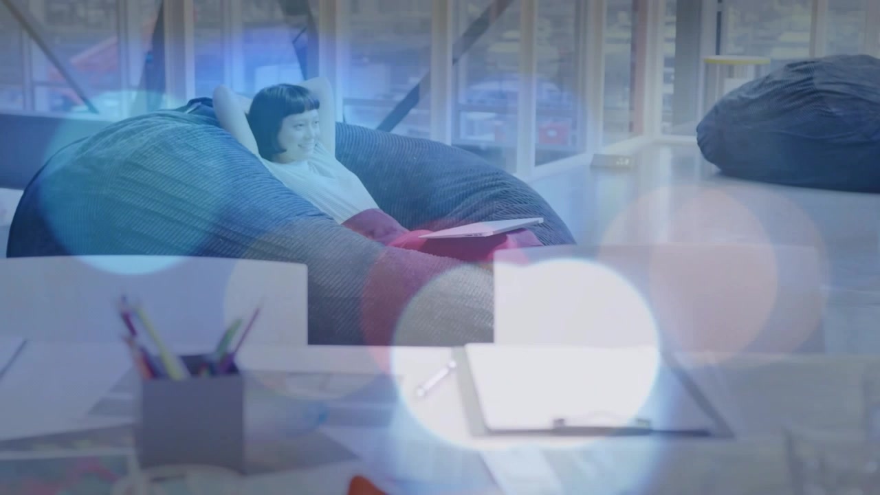코워킹 라운지에서 여성이 태블릿을 탭하여 메모를 검토하고 있으며, 보케 오버레이가 편안한 휴식 분위기를 나타냅니다.