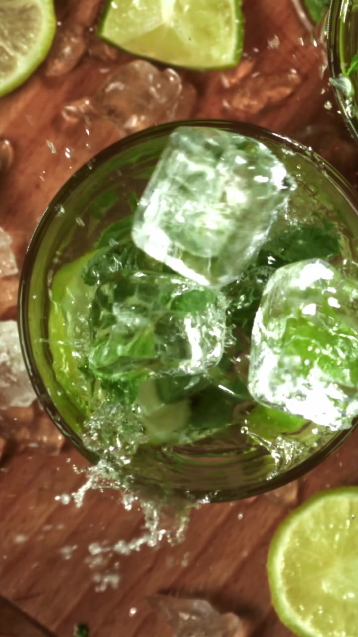 Cubetti di ghiaccio che schizzano in un rinfrescante cocktail Mojito con lime e menta