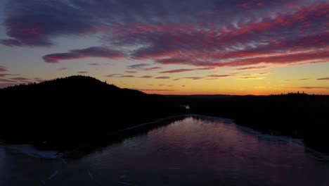 Aerial-SLIDE-high-above-frozen-pond-with-a-colorful-sunrise-reflecting-in-the-perfect-ice