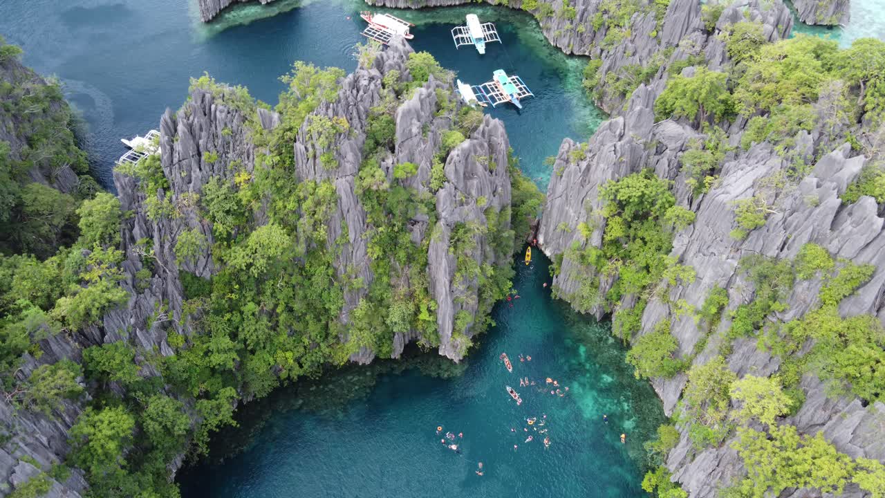 Turistas nadan en aguas cristalinas de laguna gemela entre imponentes acantilados kársticos, Coron, vista aérea