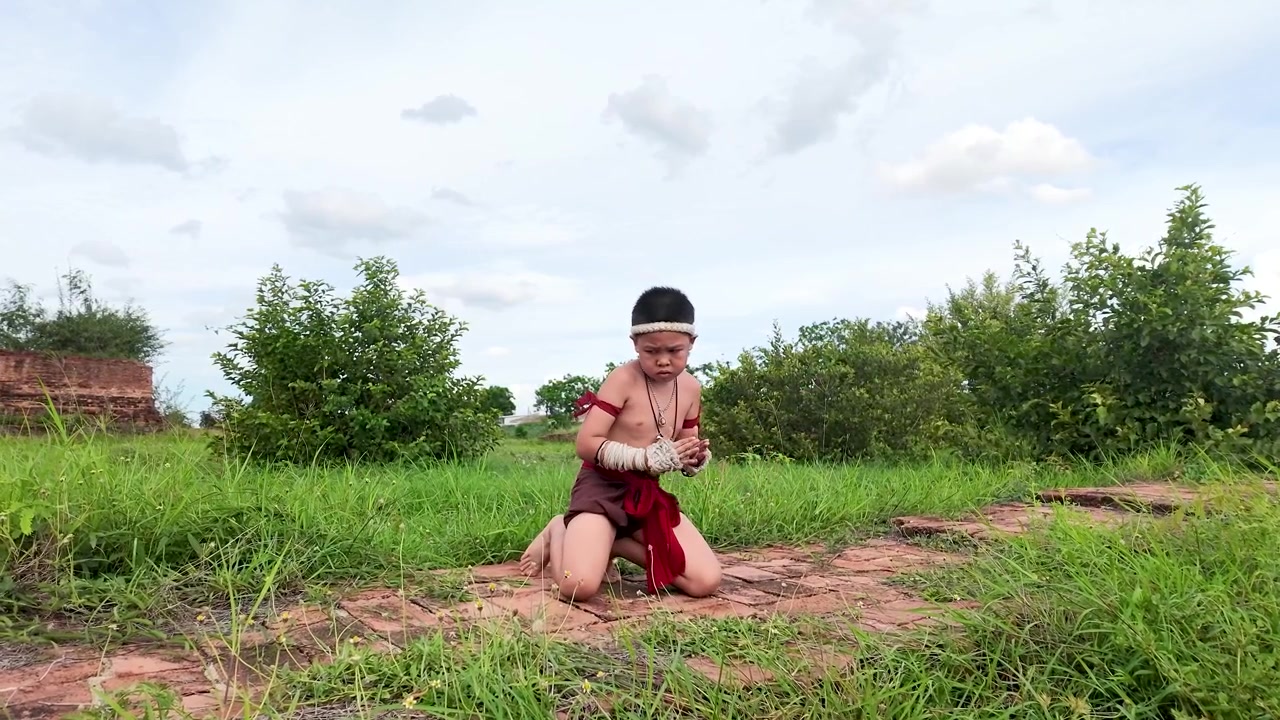 Em bé châu Á mặc trang phục truyền thống biểu diễn võ thuật ngoài trời gần tàn tích đá lịch sử