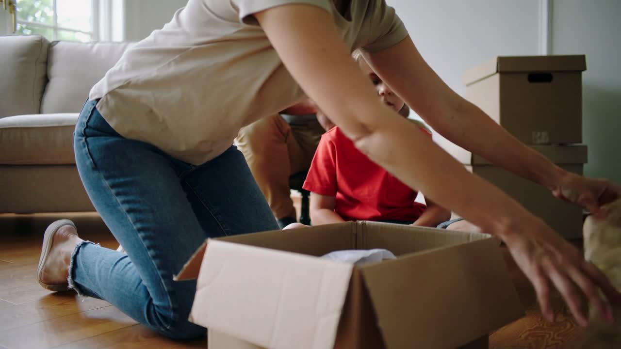 Kniende Mutter sortiert Papier und ordnet den Kartoninhalt beim Auspacken zu Hause.