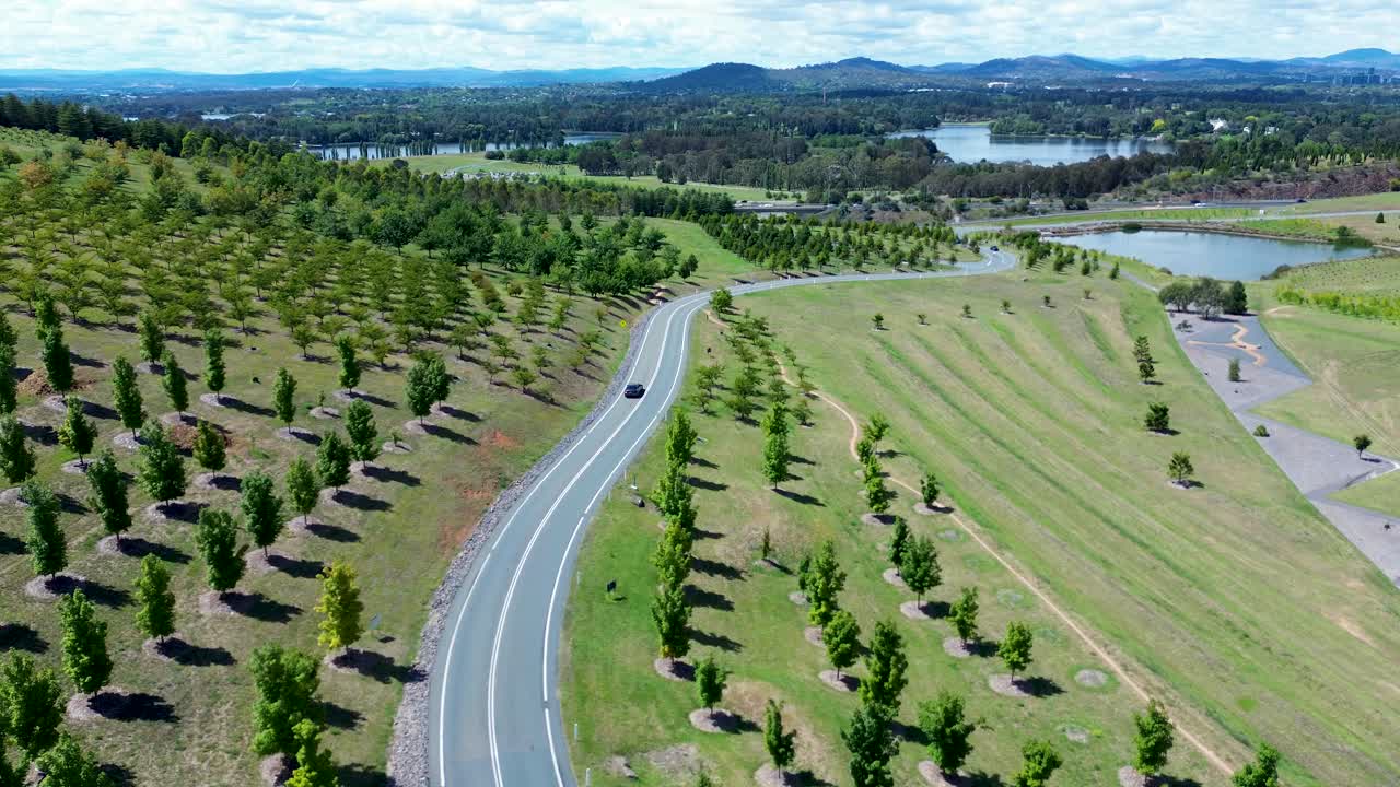 Drone aerial landscape of car vehicle travelling along town rural highway road in vineyard tree valley National Arboretum Botanical Gardens Canberra ACT Australia travel tourism transport