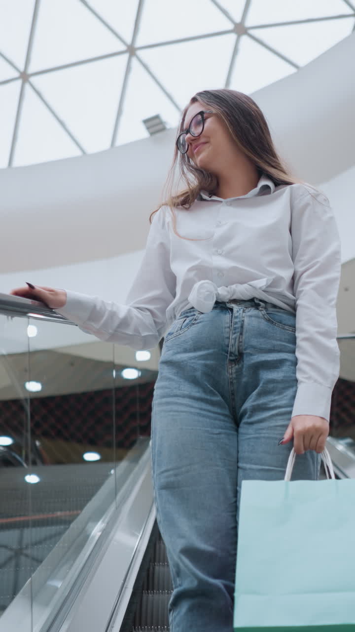joven con bolsas de compras se sube a la escalera mecánica descendente en un centro comercial moderno, colocando la mano en el riel mientras mira a la distancia, rodeada de luces brillantes
