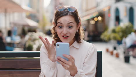 amazed woman use smartphone celebrating win good message news lottery jackpot victory in city street