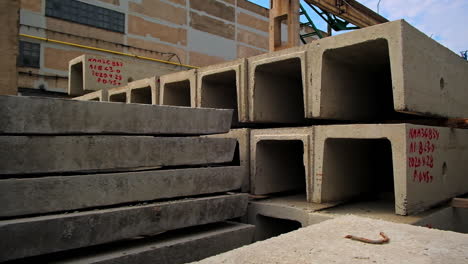 long ferroconcrete beams with metal loops on top. diverse building materials for construction outdoors. old warehouse at backdrop.