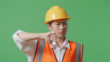 close up of asian female engineer with safety helmet showing thumbs down gesture and shaking her head while standing in the green screen background studio