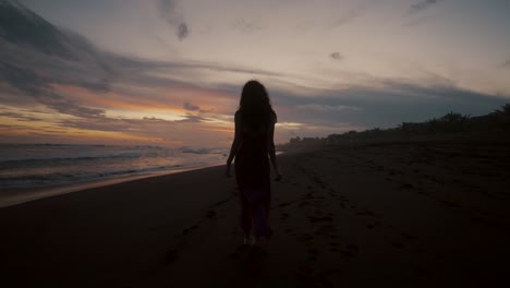a woman walking alone on the shore during sunset in summertime