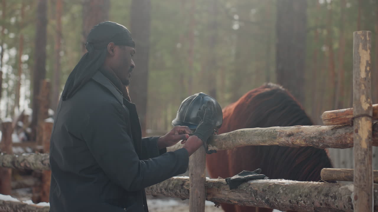 Un granjero cuida de un caballo al aire libre; un hombre atiende pacíficamente a un caballo en una escena invernal estable; un ranchero negro alimenta y acaricia cuidadosamente a un caballo en medio de un entorno nevado tranquilo y la luz de la mañana.