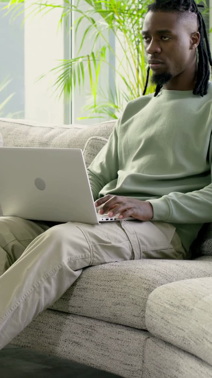 Vertical video: Typing man in sweatshirt pausing to glance then resuming typing on laptop at home