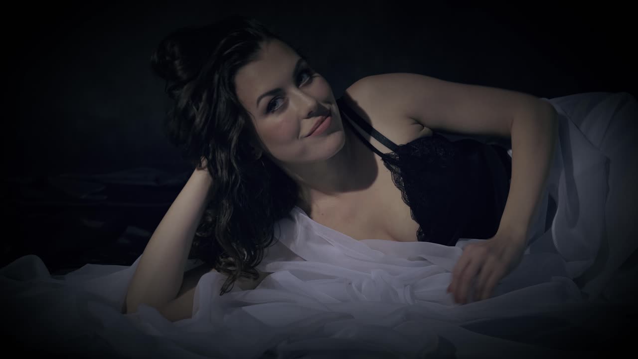Donna sensuale nel letto si siede e sorride con attesa allo spettatore