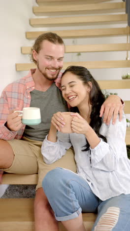 vertical video: smiling couple sitting on stairs, enjoying coffee at home, relaxing together