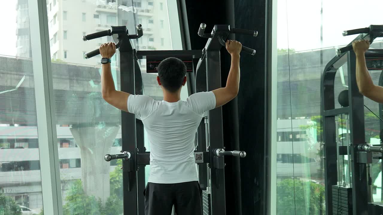 Man using assisted pull-up machine in a modern Bangkok gym with city views