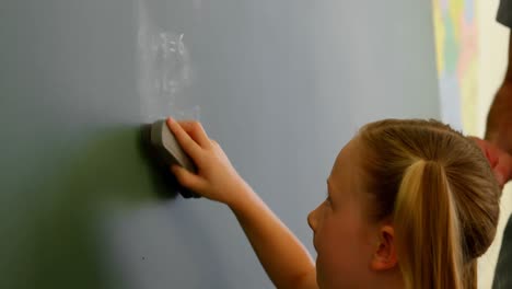 schoolgirl cleaning chalkboard with a duster in a classroom at school 4k