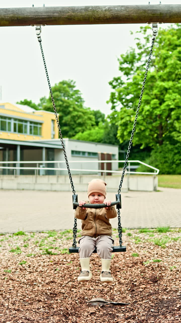 Un bambino allegro si dondola sull'altalena per strada. Il bambino si dondola sull'altalena al parco giochi. Divertimento per i bambini in un parco giochi cittadino. Il bambino gioca per strada. Sviluppo del bambino.