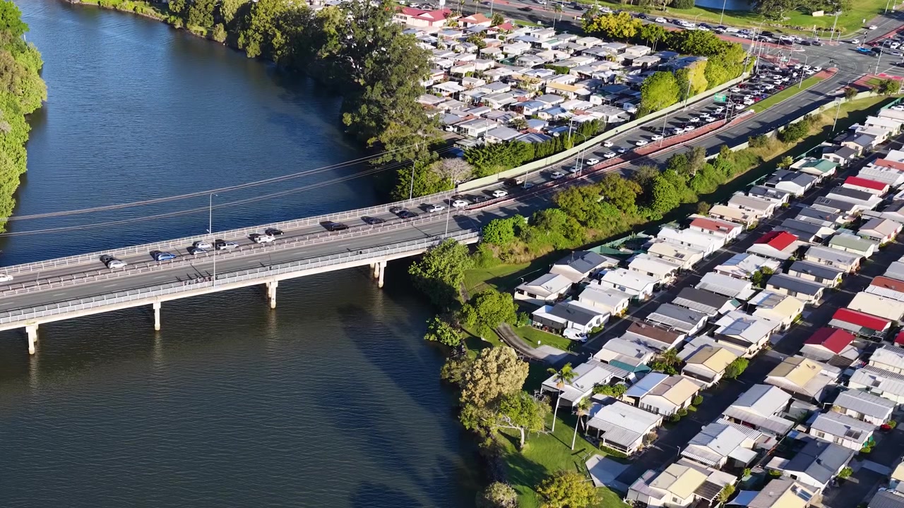 Ripresa aerea con drone di auto che attraversano un ponte fluviale accanto a un campeggio affollato.