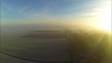 aerial of sunrise through fog above a frozen landscape