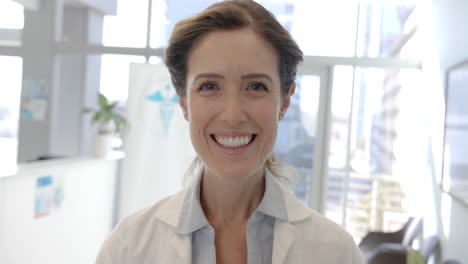 Portrait-of-happy-caucasian-female-doctor-smiling-in-hospital-reception,-slow-motion