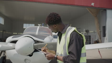 technician inspecting aircraft propeller and making notes outside hangar