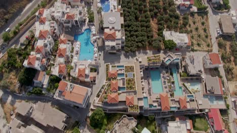 rooftops of resort town with blue pools and beautiful highway road, aerial drone tilting up view