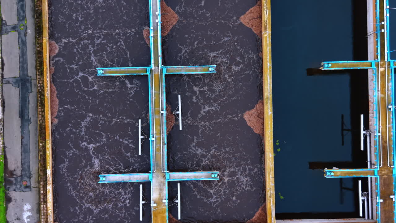 Processo di aerazione in vasche di depurazione. Superficie dell'acqua gorgogliante in vasche industriali rettangolari con passerelle metalliche blu.