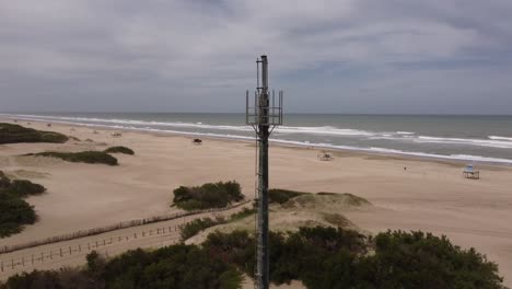 Aerial-orbiting-around-antenna-on-deserted-beach,-Mar-de-las-Pampas-in-Argentina