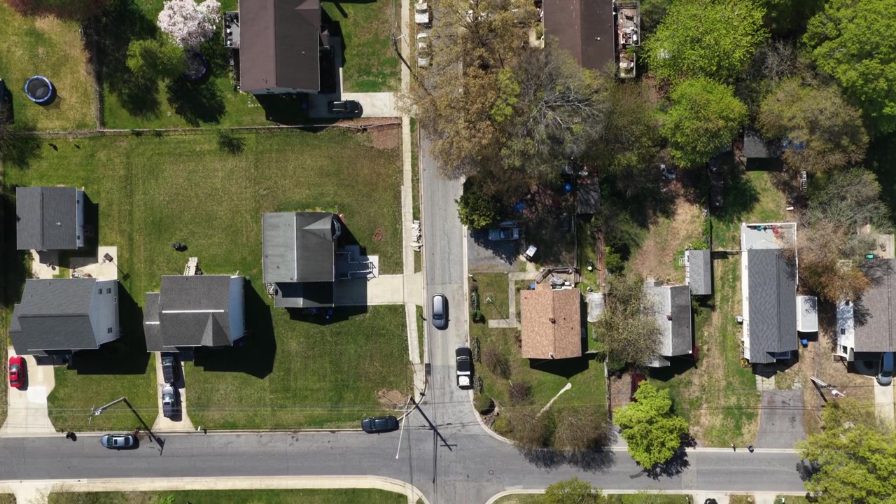 Quartiere residenziale negli USA con case unifamiliari, tetti, giardini, auto parcheggiate e un tranquillo layout stradale circondato da alberi verdi e fogliame primaverile in un ambiente residenziale calmo. Vista aerea con drone.