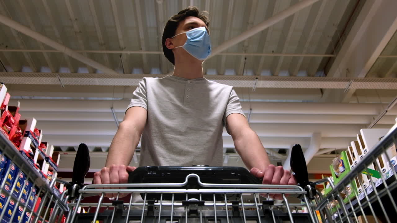 CHISINAU, MOLDOVA - JUNE 5, 2020: Young man with a protective medical mask walking in a supermarket and looking around. View from the cart. Corona Virus idea