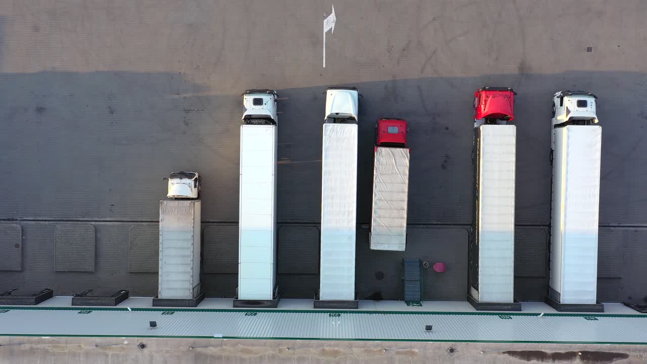 많은 트럭이 상품을 하역하고 있는 산업 창고 보관 건물 적재 구역을 떠나는 세미 트레일러가 부착된 트럭의 항공 샷