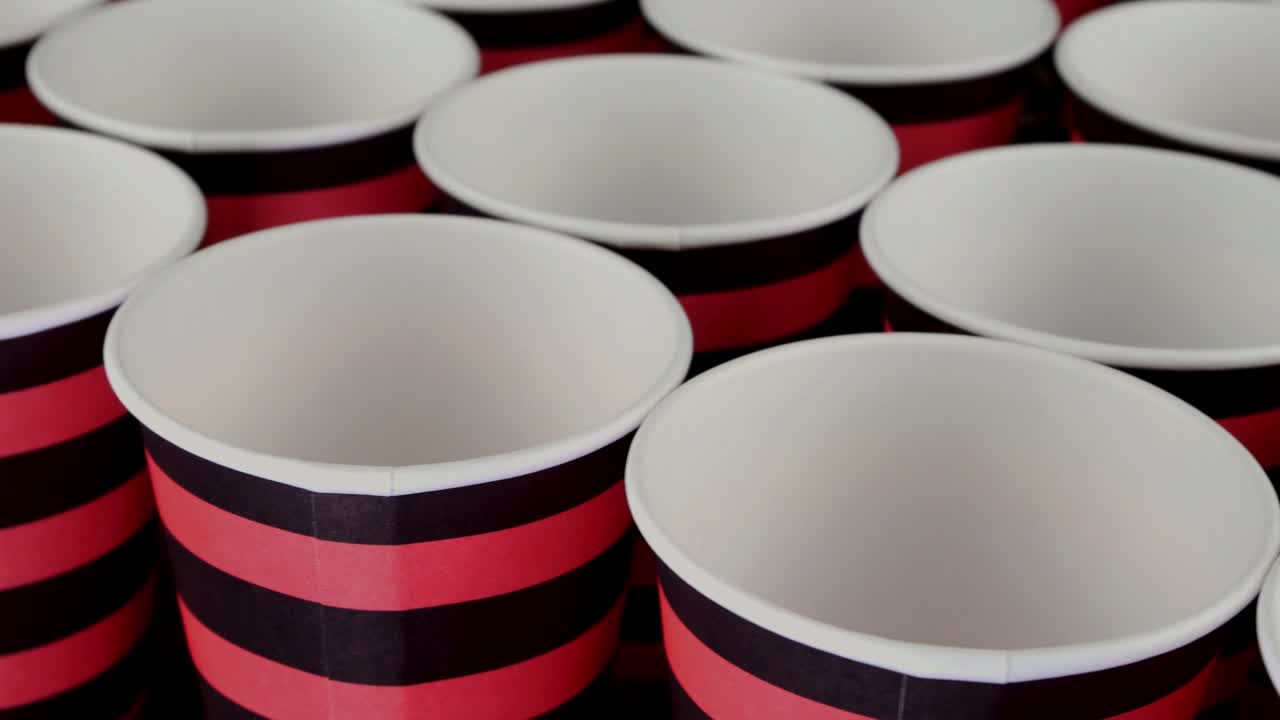 fila de taza de papel desechable roja y negra para café o bebida caliente sobre un fondo oscuro girar lentamente.