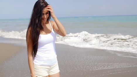 brunette woman walking on beach with hand in hair