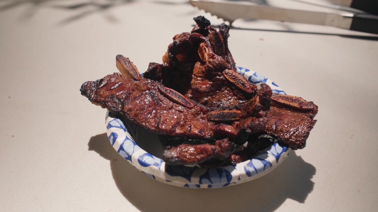 Costine di manzo tenere e cotte con una crosta scura e affumicata sono impilate su un piatto di carta e pronte per essere servite a un barbecue.