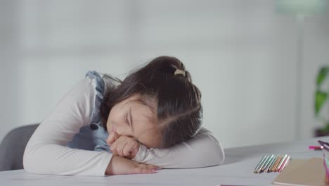 studio shot of bored hyperactive girl sitting at table at home with colouring pencils 1