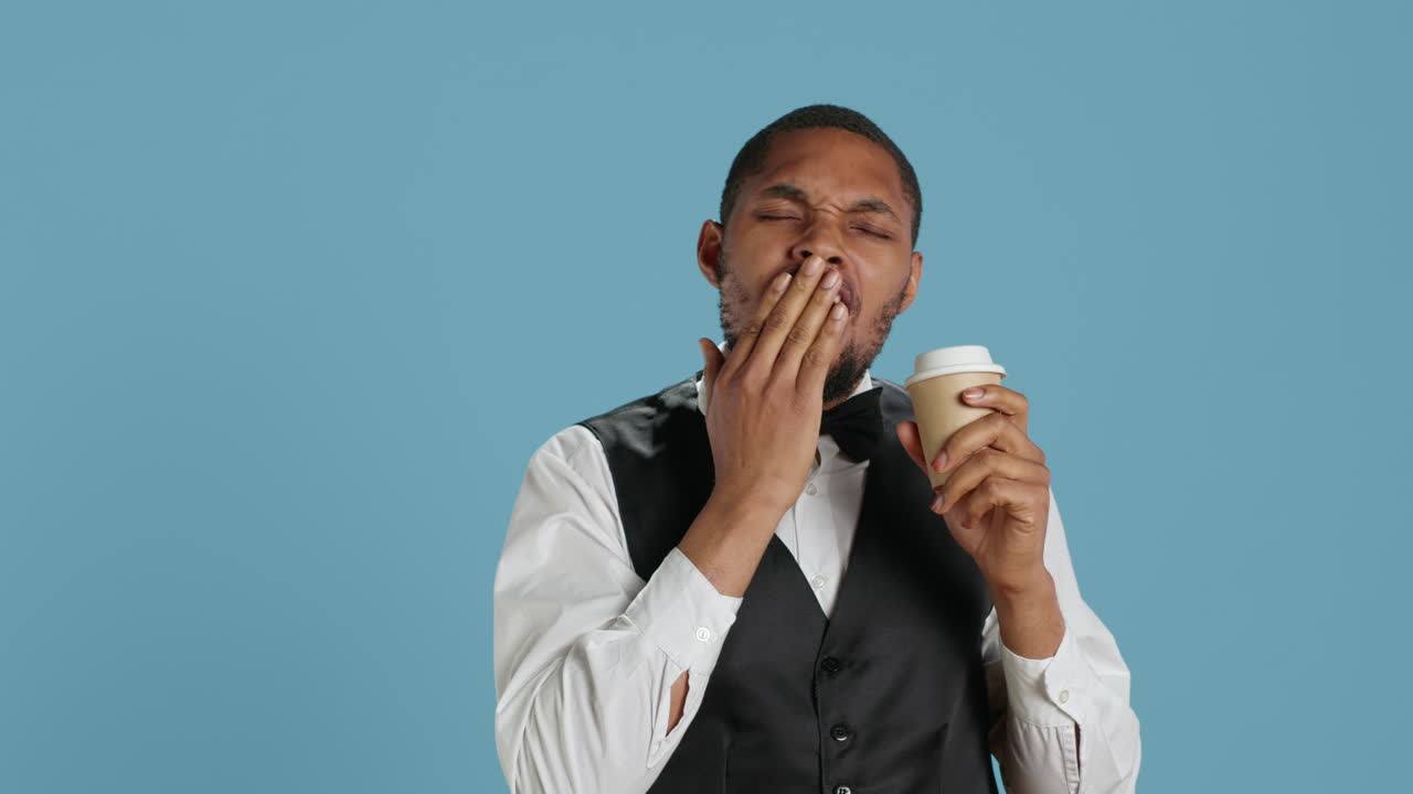 Hotel concierge staff drinks coffee while he is yawning and feeling tired